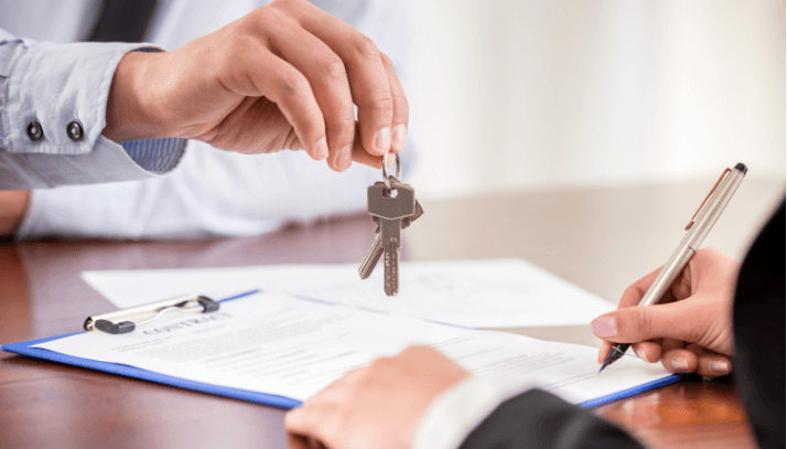 Closeup of a real estate professional handing keys to a person signing a contract