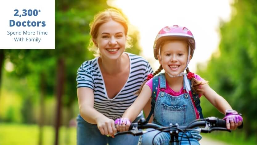 Smiling mother guides her daughter, who is wearing a helmet, on a bicycle in a sunny park