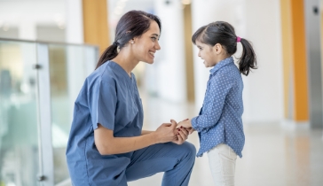 A local doctor kneeling down to hold child's hand