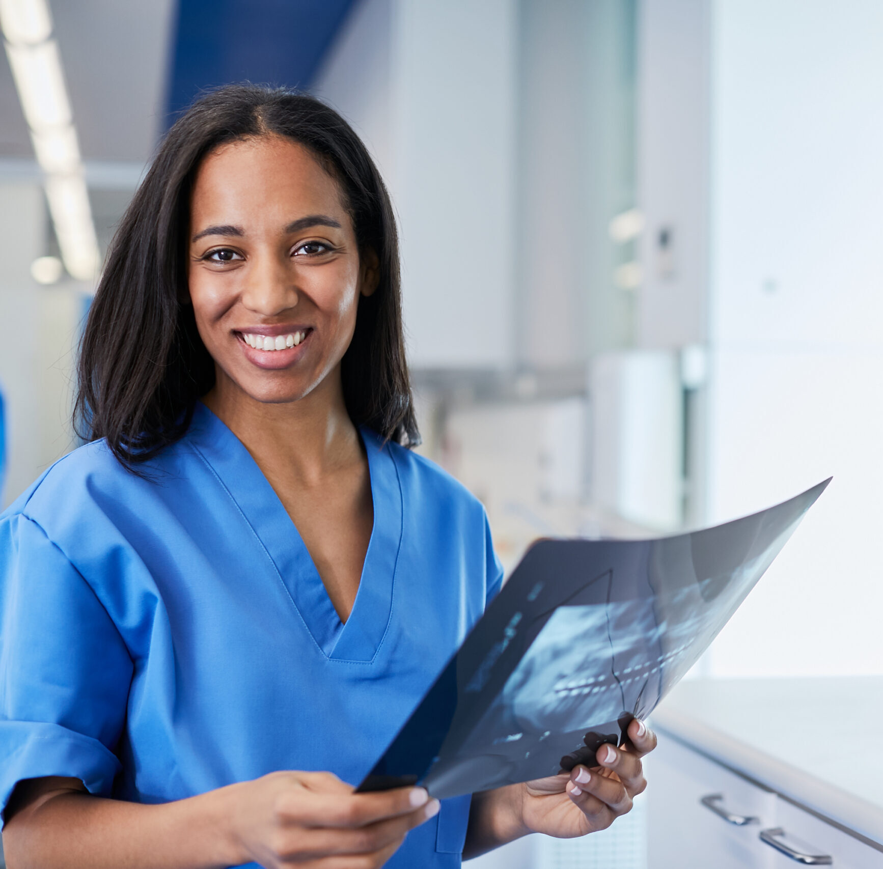 Dental assistant in blue scrubs smiling and holding dental x-ray